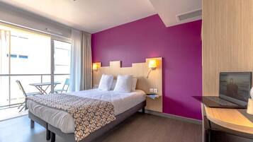 A hotel room with a large bed, a desk with a laptop, and a view of the outdoors.
