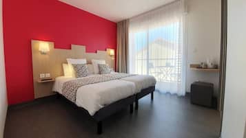 Une chambre d’hôtel moderne avec un grand lit, un mur d’accent rouge et une vue sur un immeuble à travers des rideaux transparents.
