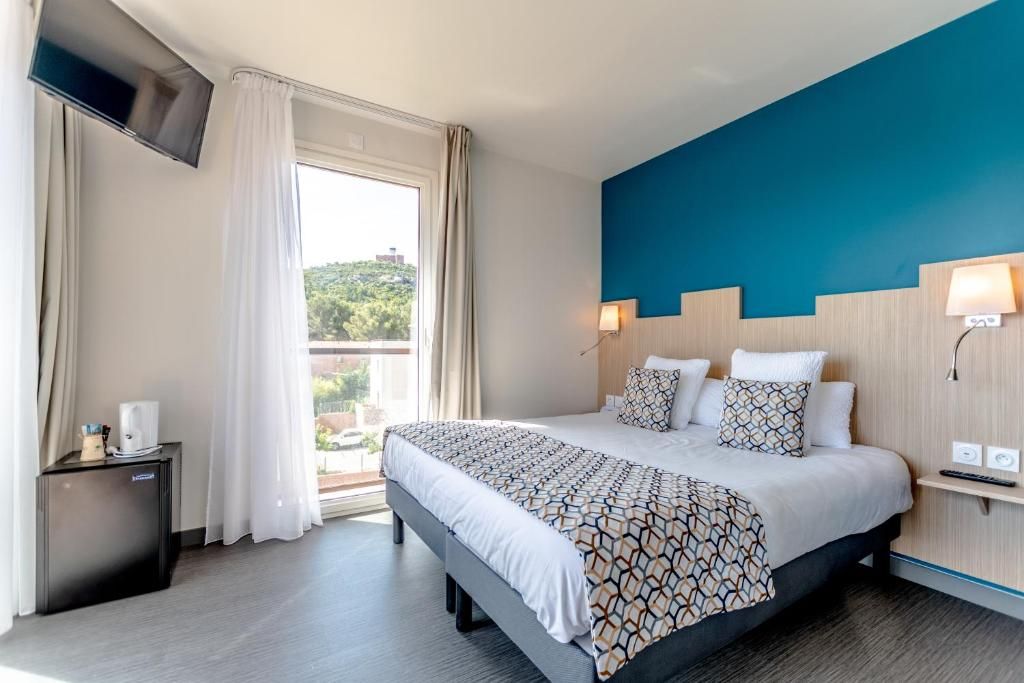 A hotel room with a large bed, a TV mounted on the wall, a small bedside table, and a window with curtains.