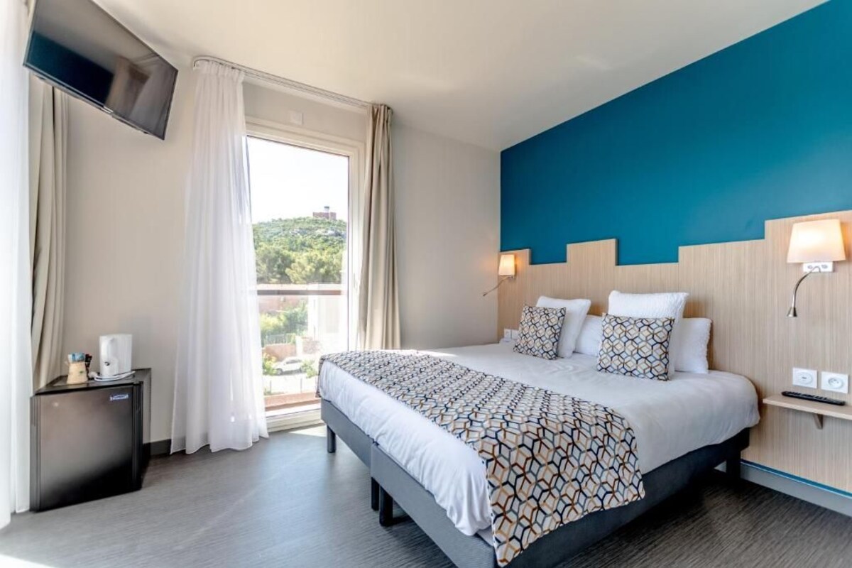 A hotel room with a large bed, a TV mounted on the wall, a small bedside table, and a window with curtains.