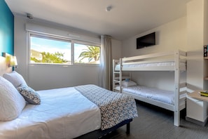 A hotel room with a bed, a bunk bed, a desk, a TV, and a window with a view of palm trees. - Hotel Le Virevent (Saint-Raphael)