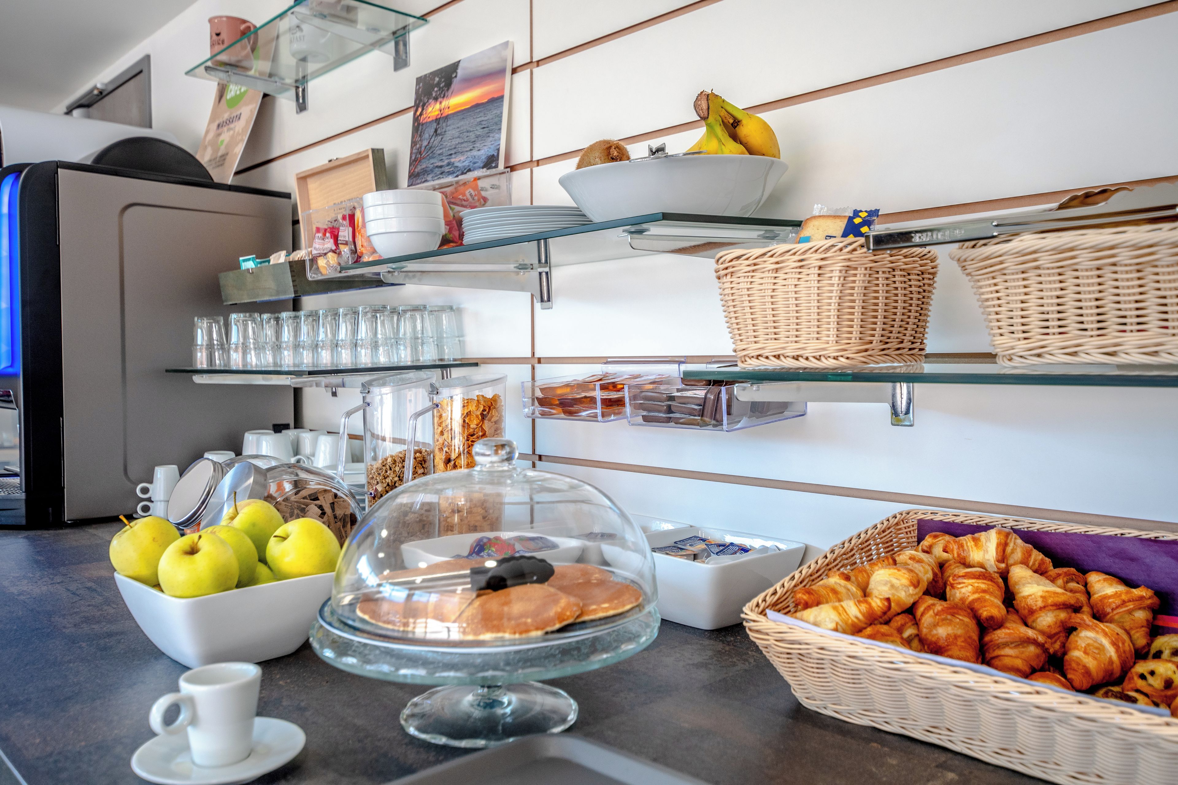 A buffet with various food items, including apples, pastries, and a covered display case.