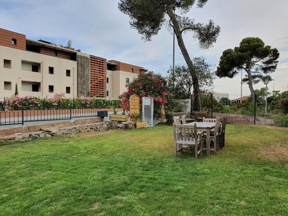 A residential area with a grassy lawn, a wooden table and chairs, and a building with balconies and a stone wall.