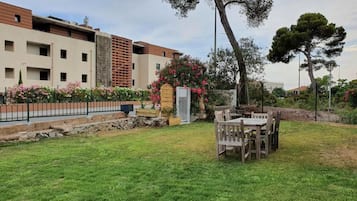 A residential area with a grassy lawn, a wooden table and chairs, and a building with balconies and a stone wall.