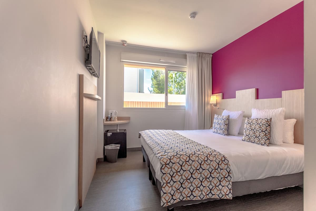 A hotel room with a bed, a small bedside table, a window, and a bathroom.