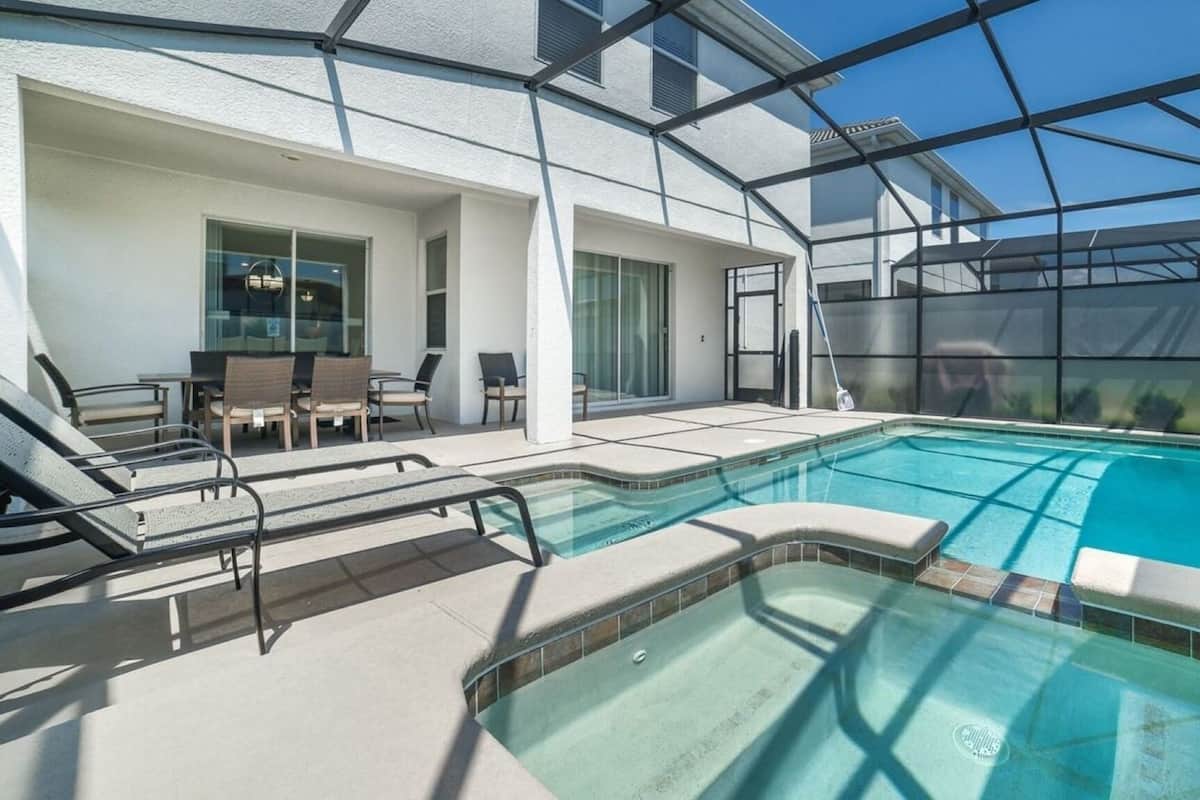 A swimming pool with a glass enclosure, lounge chairs, and a patio area.