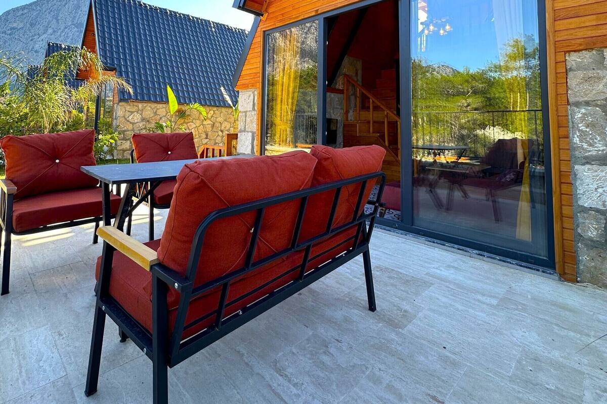 A modern house with a sloped roof, large glass doors, and a patio with red furniture.