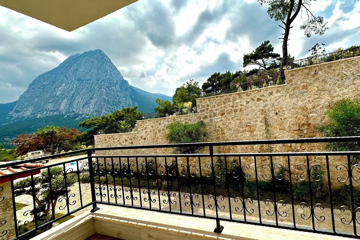 A stone wall with a metal railing, a mountain in the background, and a clear sky.
