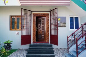 A building entrance with a wooden door, a staircase with red railings, and a small garden area with plants. - Sri Sakthi Residence (Tiruvannamalai)