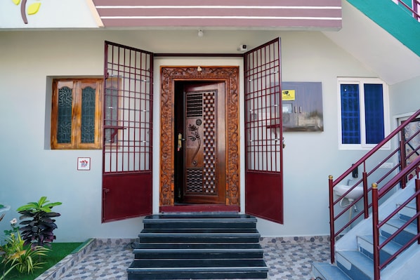 A building entrance with a wooden door, a staircase with red railings, and a small garden area with plants. - Sri Sakthi Residence (Tiruvannamalai)