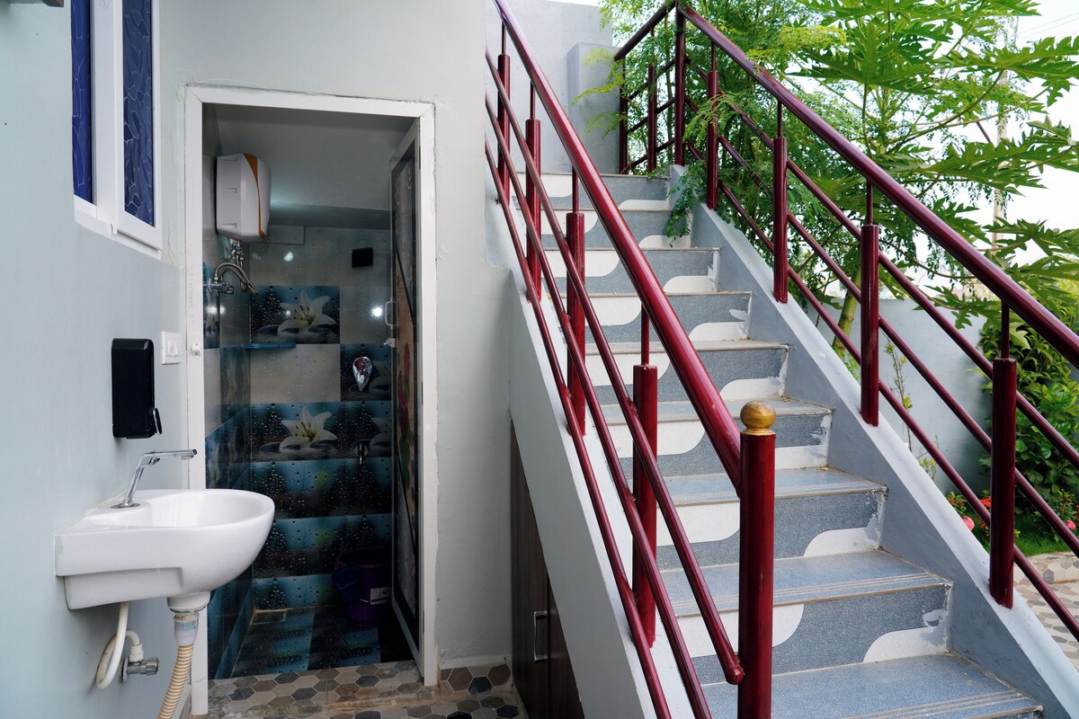 A staircase with red railings leading to a room with a white sink and a shower with a blue and green patterned shower curtain.