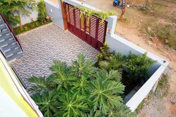 A courtyard with a patterned floor, a red gate, and lush greenery including large-leafed plants. - Sri Sakthi Residence (Tiruvannamalai)