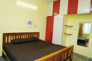 A single bed with a wooden headboard in a room with a yellow wall and a red and white wardrobe. - Sri Sakthi Residence (Tiruvannamalai)