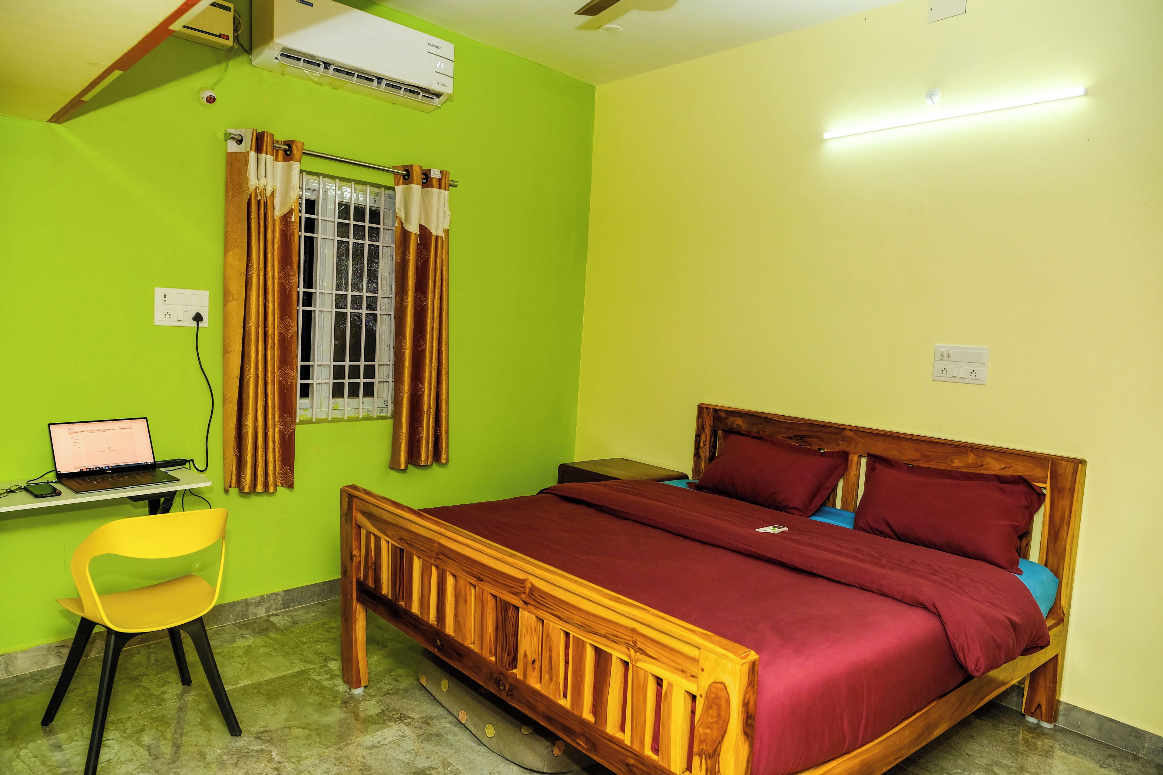 Una habitación con una cama de madera, un escritorio con una computadora portátil, una silla y una ventana con cortinas.