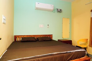 A single bed with a wooden headboard, a wall-mounted air conditioner, a power outlet, and a yellow chair. - Sri Sakthi Residence (Tiruvannamalai)