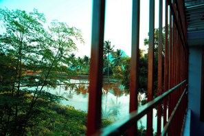 A view through a metal fence with a body of water, trees, and a distant structure.
