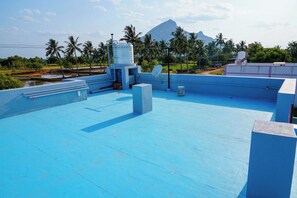 A rooftop terrace with a blue floor, satellite dish, water tank, and a mountain in the background.