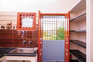 A compact kitchen with a sink, a window with bars, and a view of greenery outside.