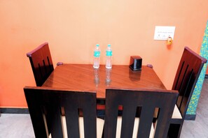 A wooden dining table with two water bottles, a small speaker, and a power outlet on the wall. - Sri Sakthi Residence (Tiruvannamalai)