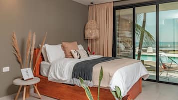 Quarto moderno com uma cama grande, uma mesinha de cabeceira e vista para o oceano através de grandes portas de vidro.