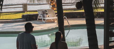 A pool area with lounge chairs, palm trees, and a concrete walkway.