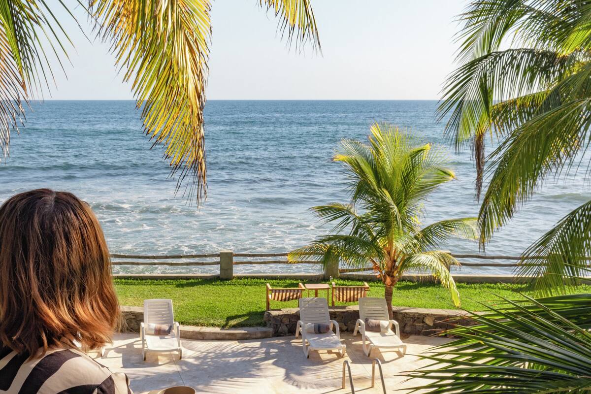 Ein Poolbereich mit Liegestühlen, einer Palme und Blick auf das Meer.