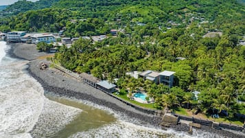 Vista aérea de una zona costera con playa, un litoral rocoso y una colina con vegetación densa.