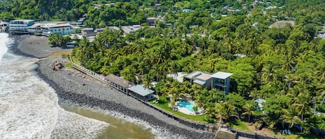 An aerial view of a coastal area with a beach, a rocky shoreline, and a hill with dense vegetation.