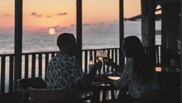 Ein Paar speist in einem Restaurant am Meer mit Blick auf den Sonnenuntergang über dem Ozean.