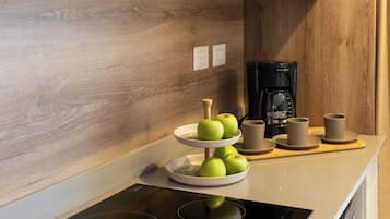 Una cocina con una placa de inducción moderna, una cafetera y una exposición de frutas.