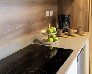 Uma cozinha com um fogão por indução moderno, uma cafeteira e uma seleção de frutas.