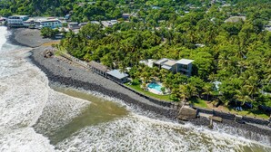 An aerial view of a coastal area with a beach, a rocky shoreline, and a hill with dense vegetation. - Fishermans Resort Life (La Libertad)