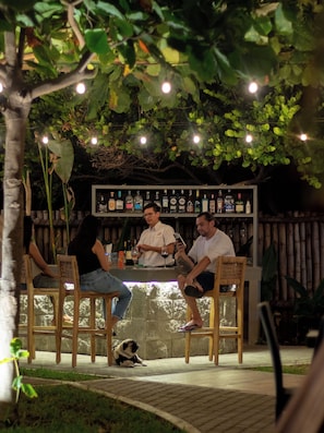 Una zona de bar con sillas de madera, una barra con botellas y un perro pug en el suelo.
