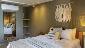A modern bedroom with a large bed, a wall-mounted air conditioner, and a mirror reflecting the room.