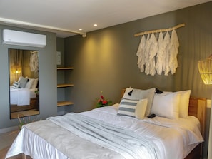 A modern bedroom with a large bed, a wall-mounted air conditioner, and a mirror reflecting the room.