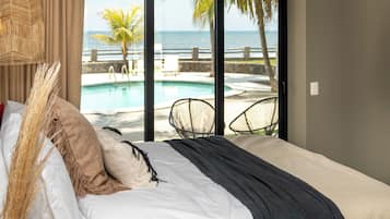 Ein Schlafzimmer mit Bett, Blick auf Pool und Strand sowie einem großen Fenster.