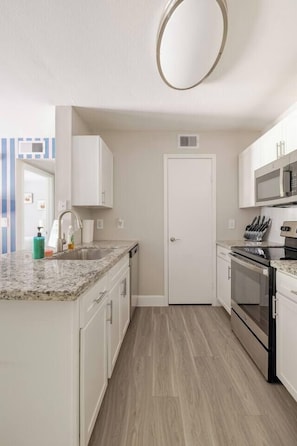 Eine kompakte Küche mit weißen Schränken, einer Edelstahlspüle, einer Mikrowelle und einem Backofen.