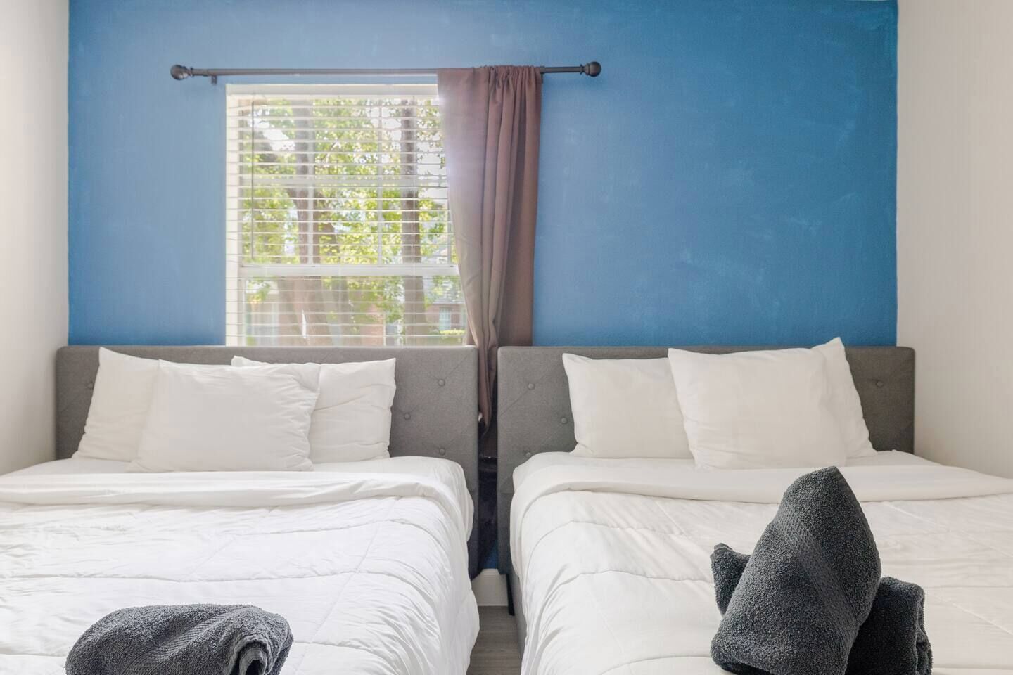 A room with two beds, a window with blinds, and a curtain.