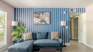 Un salon avec un canapé bleu, un mur à rayures et un tableau.