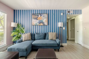 Ein Wohnzimmer mit blauem Sofa, gestreifter Wand und einem Gemälde.