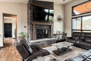 A living room with a stone fireplace, leather sofas, a marble coffee table, and a large window.
