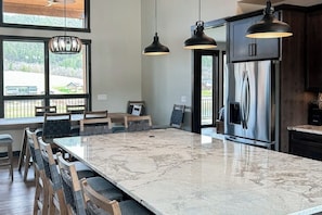 A kitchen with a large marble island, dark cabinetry, and pendant lighting.