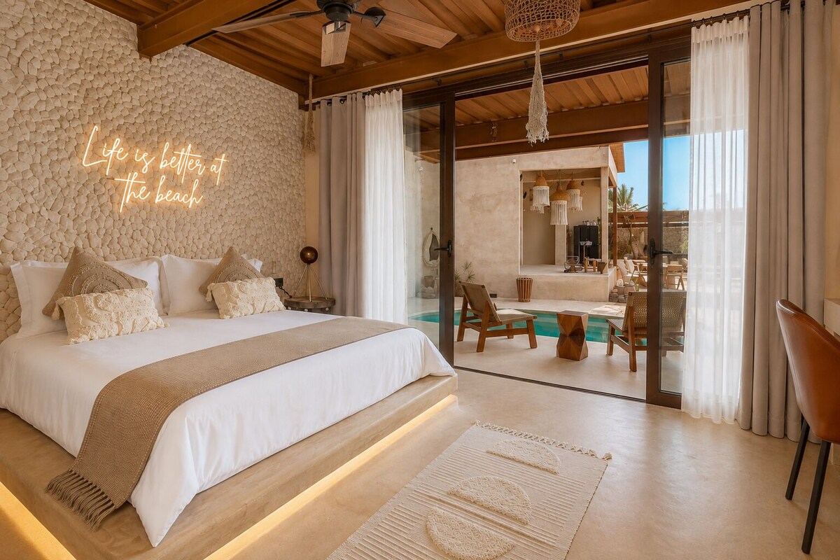 Ein Schlafzimmer mit einem großen Bett, Blick auf den Pool und einem Neonzeichen.