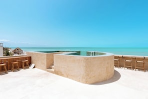 Un bar en la azotea con piscina, sillas de madera y vistas al océano.