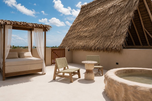 Un espacio al aire libre con techo de paja, que incluye una cama, sillas, una mesa y un jacuzzi.