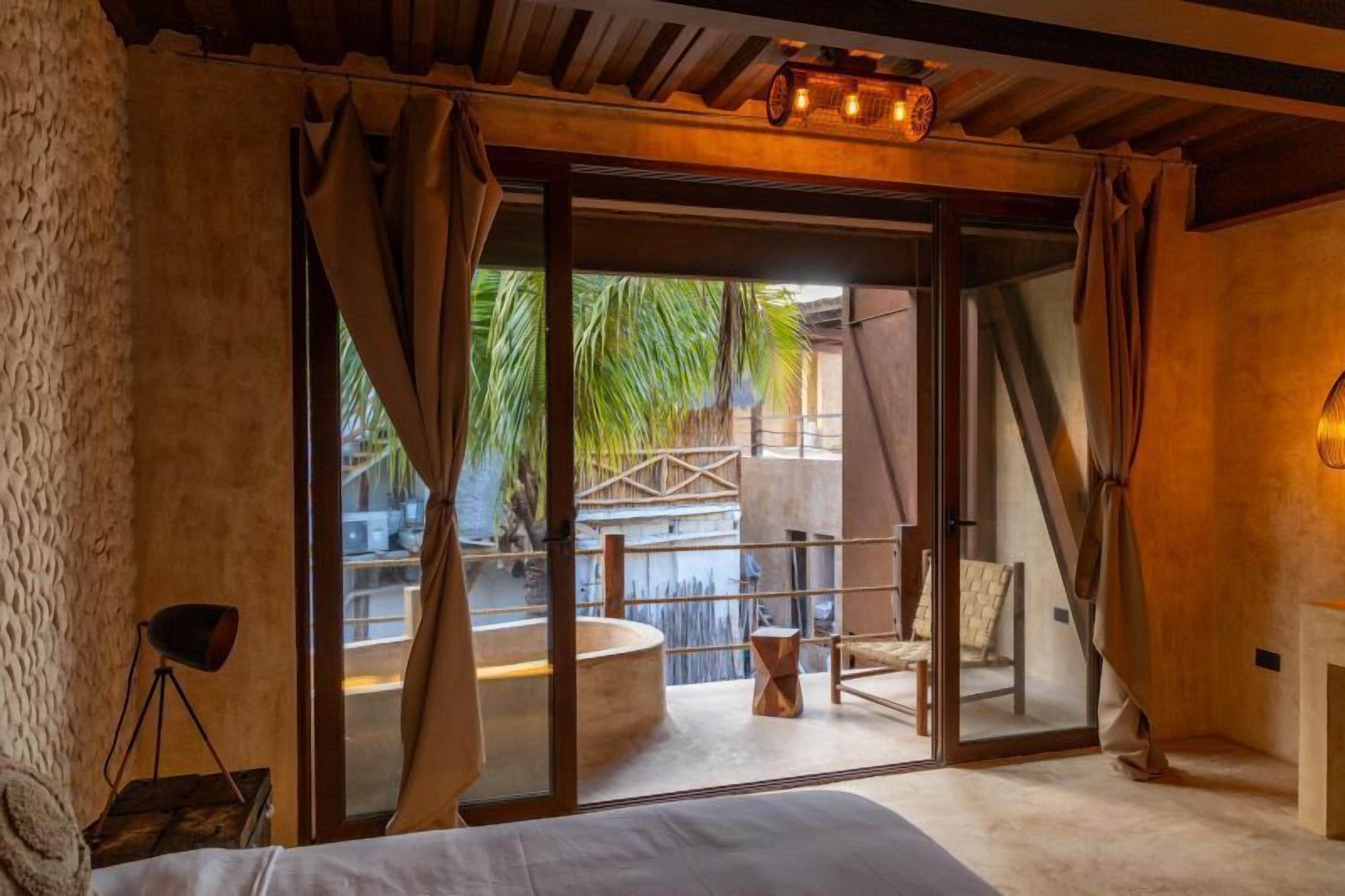 Une chambre moderne avec un lit, une petite table, une chaise et une vue sur une piscine et des palmiers.