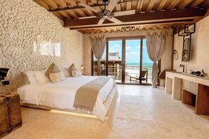 A bedroom with a large bed, a ceiling fan, a stone wall, and a view of the ocean. - Awa Holbox Hotel Boutique - Beach Front (Isla Holbox)