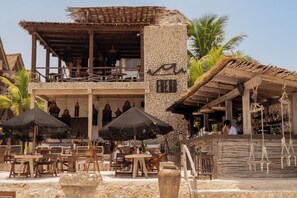 Un restaurant situé en bord de mer, doté d’une terrasse, de murs en pierre et d’un toit de chaume.