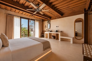 Un dormitorio con una cama grande, un ventilador de techo, un baño con tocador y vistas a palmeras.