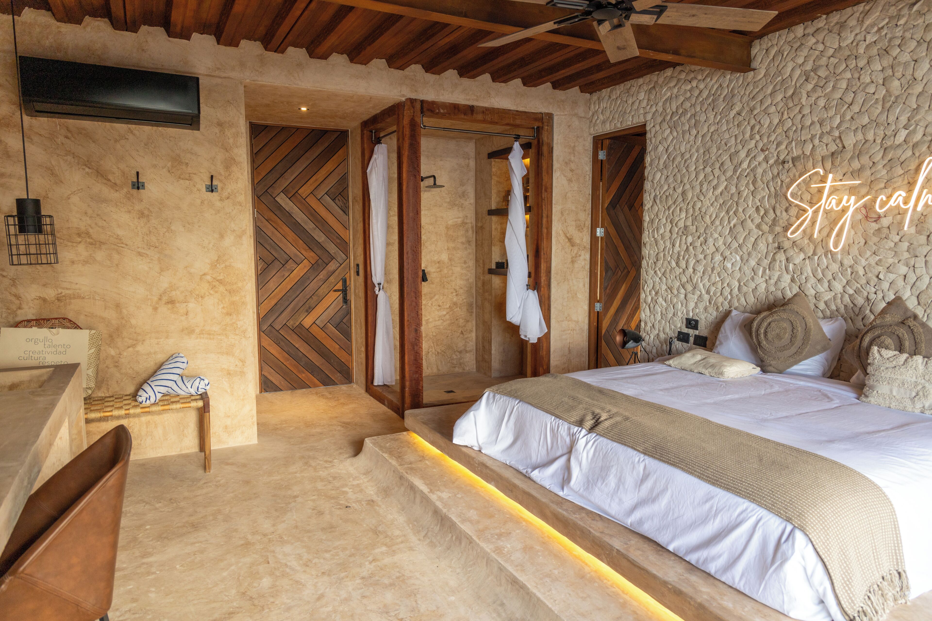 Une chambre avec un lit, un banc en bois, un banc avec une serviette, et un mur orné d’un motif en chevrons.